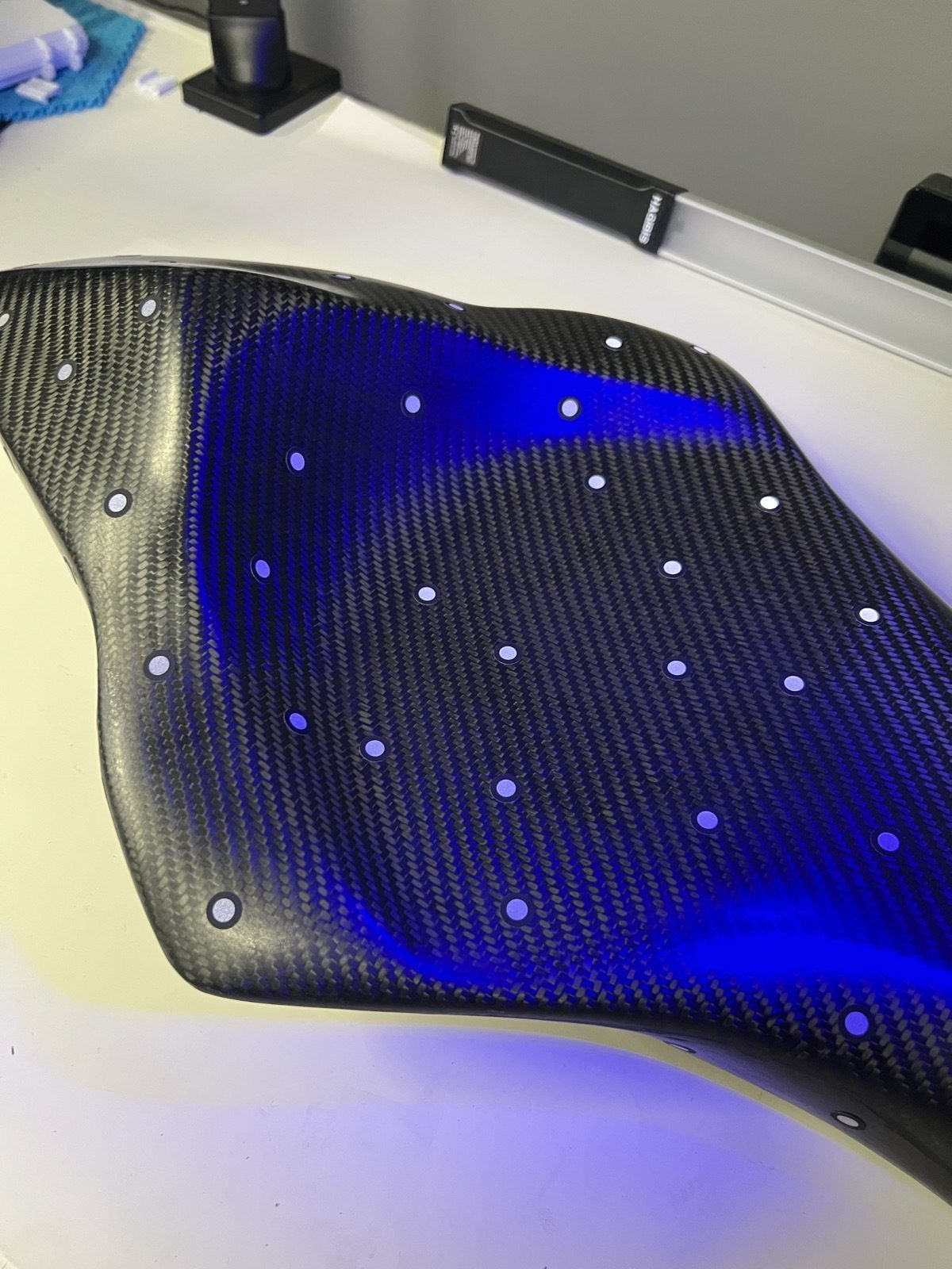 Carbon fibre race motorcycle seat with reference dots under blue structured-light scanning